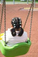 enfant ayant amusement sur une balançoire sur le terrain de jeux dans Publique parc. photo