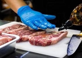 le chef coupe la viande crue avec un couteau sur une planche, le cuisinier coupe la viande crue