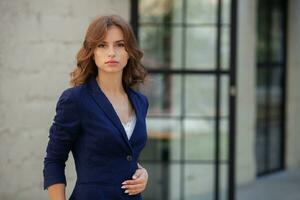 portrait de une réussi affaires femme dans de face de moderne affaires bâtiment. Jeune directeur pose dehors. femme employé de un bureau. photo