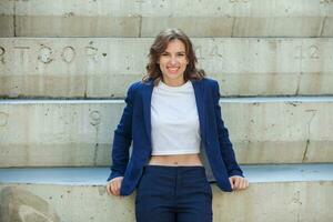 portrait de une réussi affaires femme dans de face de moderne affaires bâtiment. Jeune directeur pose dehors. femme employé de un bureau. photo