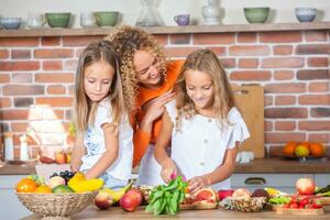 mère et filles cuisine ensemble dans le cuisine. en bonne santé nourriture concept. portrait de content famille avec Frais smoothies. content sœurs. photo