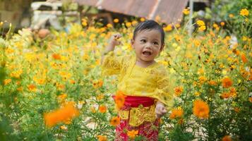 peu mignonne fille portant Jaune balinais robe en jouant dans Jaune et blanc fleur jardin photo