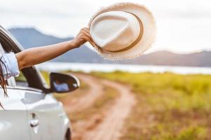 Happy woman hand holding hat à l'extérieur de la voiture fenêtre ouverte