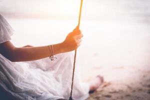 main de femme asiatique en robe blanche assise sur une balançoire à la plage photo