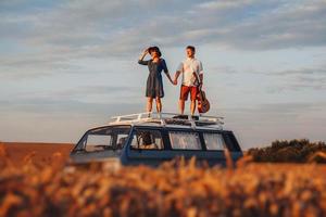 homme avec une guitare et femme debout sur le toit d'une voiture dans un champ de blé photo