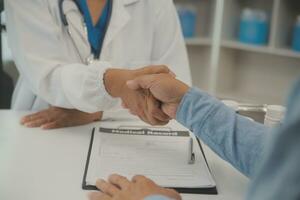 souriant Jeune femelle médecin secouer main proche santé Assurance traiter avec personnes âgées patient à consultation dans hôpital. content femme gp poignée de main salutation avoir connaissance avec mature homme dans clinique. photo