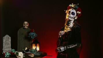 femelle modèle portant Père Noël muerte corps art dans studio, agissant glamour sur journée de le mort mexicain Halloween fête. rituel crâne corps art, posant avec noir des roses et fleurs couronne. photo