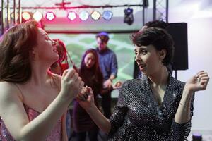 Jeune caucasien femmes dansant à vivre la musique performance dans boîte de nuit. deux copines faire la fête et aller en boîte sur piste de dance ensemble, profiter vie nocturne divertissement activité photo