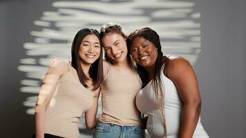 diverse copains agissant de bonne humeur à propos corps acceptation dans studio, sentiment magnifique et La publicité soin de la peau campagne. Jeune glamour femmes souriant sur caméra et promouvoir corps positivité. photo