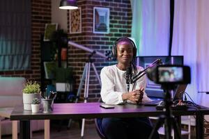 africain américain vlogger enregistrement l'Internet spectacle en utilisant moderne caméra, parlant à propos histoire sujets. influenceur tournage vivre diffuser en utilisant professionnel dispositifs dans vivant pièce studio photo