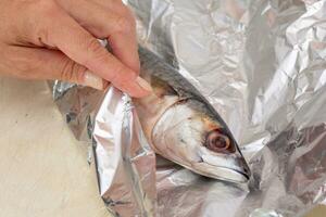 femme main emballage dans papier d'aluminium entier brut maquereau poisson photo