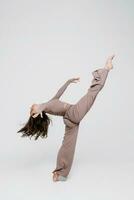 une magnifique mince gymnaste dans une survêtement est Faire jambe diviser, élongation, yoga dans une blanc studio. photo