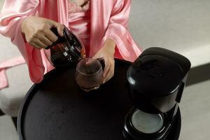 une femme est Heureusement en train de préparer café dans sa rose satin pyjamas dans le Matin. photo