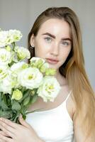 mignonne content Jeune fille en portant une bouquet et regards à le de fleurs photo