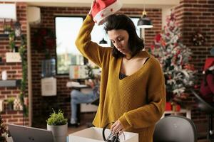 dérangé femmes ouvrier prise de Père Noël chapeau et emballage Bureau des choses dans boîte après avoir mis à la porte de emploi sur Noël veille. sans emploi la personne déchargé de travail avant Noël vacances photo