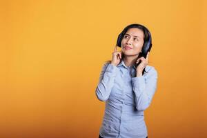 souriant joyeux femme avec écouteurs écoute musique, dansant dans studio plus de Jaune Contexte. philippin modèle ayant amusant, montrant Danse se déplace pendant Pause temps. divertissement concept photo