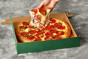 femelle main prise tranche de Pizza avec fondu mozzarella, pepperoni et jalapeno de carton boîte photo