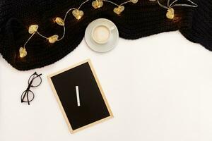 une tasse de café, une petit noir en bois planche et une blanc craie avec Nouveau ans buts. écharpe et Noël lumières sur blanc Contexte. photo