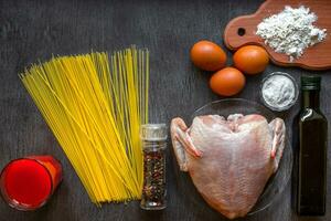 cuit spaghetti nouilles. non cuit spaghetti et brut poulet sur planche. Ingrédients pour fait maison nouilles poulet œufs, légume huile. le foncé noir bois Contexte. Haut voir. photo