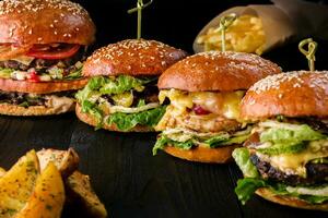 quatre fait maison hamburgers sur en bois tableau. petits pains avec sésame graines, du boeuf des hamburgers et divers ingrédients. photo