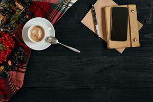 au dessus vue de intelligent téléphone avec carnet et tasse de latté café sur noir en bois Contexte. photo