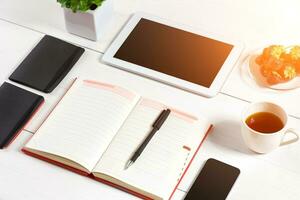 Bureau table bureau avec ensemble de fournitures, blanc Vide bloc-notes, tasse, stylo, tablette, lunettes, fleur sur blanc Contexte. Haut vue photo