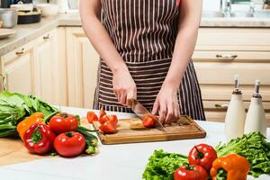 Jeune femme cuisine dans le cuisine à maison. une femme coupes une tomate et des légumes avec une couteau. photo