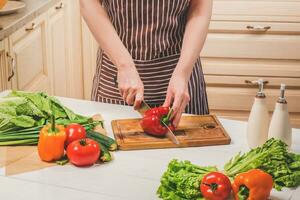 Jeune femme cuisine dans le cuisine à maison. une femme coupes une poivre et des légumes avec une couteau. photo