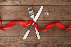 la Saint-Valentin journée dîner table réglage avec rouge ruban, couteau et fourchette bague plus de chêne Contexte. photo