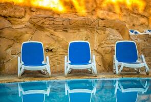 chaises longues près nager bassin et réfléchi leur dans bleu l'eau photo