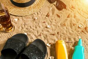 été tenue de plage, retourner flops, chapeau, du froid boisson dans une verre et coquillages sur le sable plage. photo