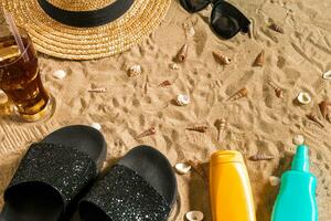 été tenue de plage, retourner flops, chapeau, du froid boisson dans une verre et coquillages sur le sable plage. photo