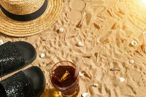 été tenue de plage, retourner flops, chapeau, du froid boisson dans une verre et coquillages sur le sable plage. photo