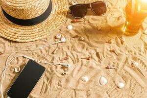 été tenue de plage, des lunettes de soleil, chapeau, du froid boisson dans une verre et coquillages sur le sable plage. photo