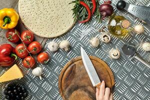 femelle main avec couteau sur métal cuisine tableau, autour mensonge ingrédients, légumes, et épices pour Pizza. photo