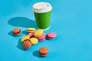 chaud café dans vert papier tasse avec blanc couvercle et macarons sur bl photo