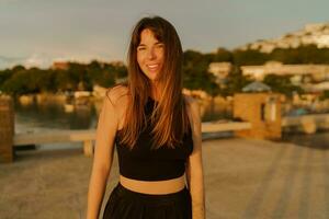 magnifique brunette femme avec élégant coiffure en marchant Extérieur sur le jetée. chaud soleil couchant couleurs. Voyage et vacances concept. photo