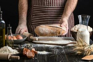 chef détient le Frais pain dans main. homme en train de préparer pâte à table dans cuisine. photo