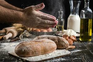 chef arrose Frais pain avec farine. homme en train de préparer pâte à table dans cuisine. photo
