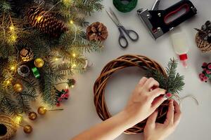 femelle mains décorer le Noël couronne avec épicéa branches avec une rouge baie et forêt cônes. blanc Contexte. Nouveau années concept. photo