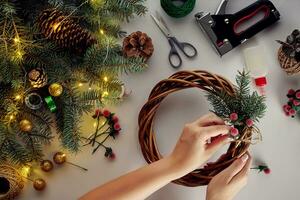 femelle mains décorer le Noël couronne avec épicéa branches avec une rouge baie et forêt cônes. blanc Contexte. Nouveau années concept. photo