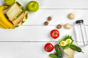 déjeuner. sandwich et Frais légumes, bouteille de eau, des noisettes et des fruits sur blanc en bois Contexte. en bonne santé en mangeant concept. Haut vue avec copie espace photo