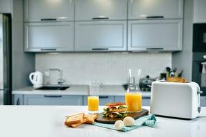 blanc électrique pain grille-pain avec Orange jus avec sandwich sur cuisine tableau. petit déjeuner dans le confortable cuisine. photo