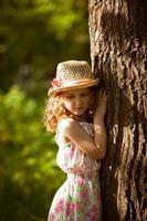 petite fille au chapeau de paille debout près d'un arbre