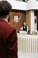 employé accueillant homme d'affaire dans lobby, fournir luxe prestations de service pour client en voyageant sur travail voyage. client en arrivant à recours avec bagages, recevoir amical assistance de Hôtel personnel. photo