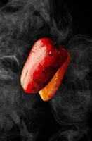 grillé rouge et Orange poivrons planant dans blanc brume sur noir Contexte photo