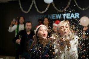 Nouveau année faire la fête, groupe de Jeune gens dans Père Noël Chapeaux soufflant confettis tandis que célébrer Nouveau année photo