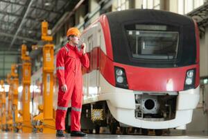 portrait de une technicien en utilisant une walkie talkie dans de face de une train pour communiquer avec le sien collègues de travail après inspecter le électrique les trains machinerie réparations. photo