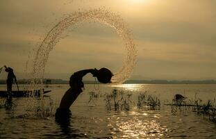 silhouette de une pêcheur dans le l'eau à coucher de soleil, Thaïlande. photo