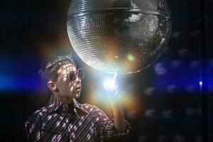 une Jeune garçon à un soir fête dans le des rayons de lumière et avec une disco balle. photo